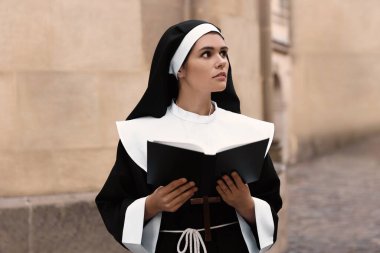 Young nun reading Bible near building outdoors