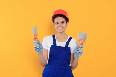 Professional worker with putty knives in hard hat on orange background