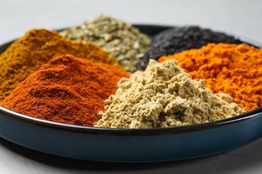 Plate with different spices on light grey table, closeup