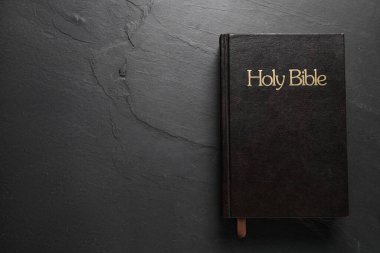 Hardcover Bible on black table, top view with space for text. Religious book