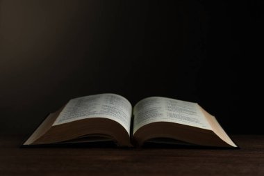 Open hardcover Bible on wooden table, space for text. Religious book