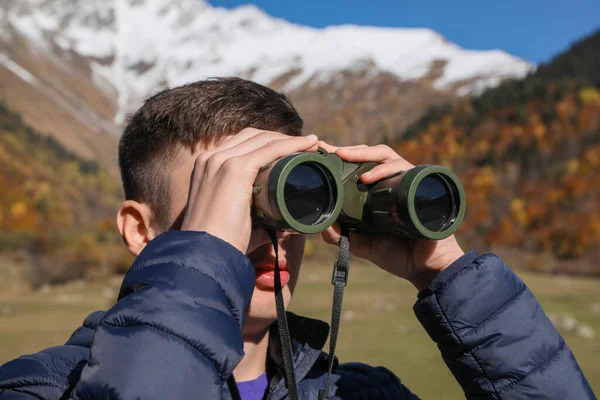 Boy looking through binoculars in mountains on sunny day