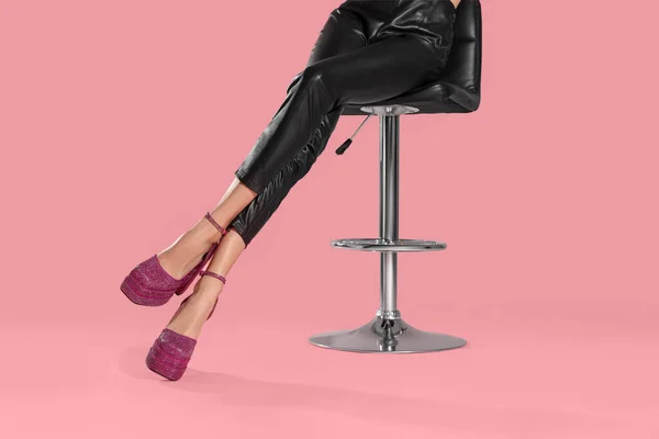 Woman wearing high heeled shoes with platform and square toes sitting against pink background, closeup