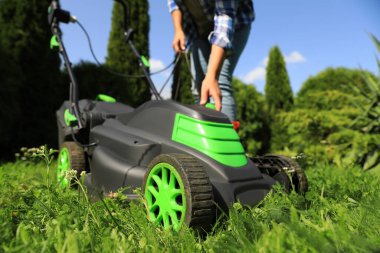 Woman turning on lawn mower in garden, closeup. Cutting grass