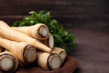 Whole raw parsley roots and fresh herb on brown table, closeup. Space for text