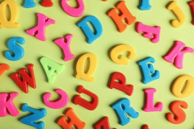 Many colorful magnetic letters on light green background, flat lay