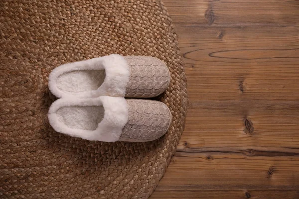 Pair of warm stylish slippers and wicker mat on wooden floor, flat lay. Space for text