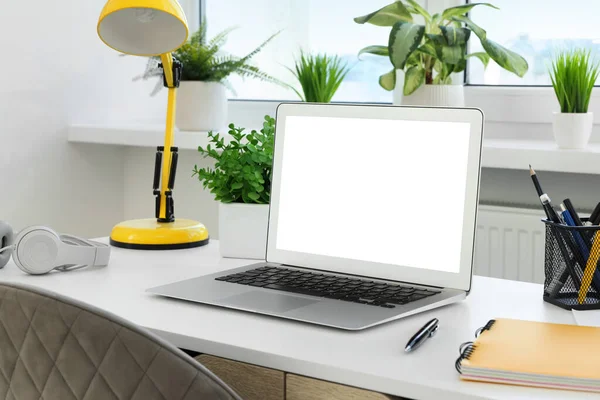 Comfortable workplace at home. Modern laptop with blank screen and lamp on white desk. Mockup for design
