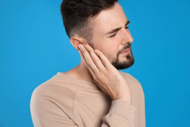 Young man suffering from ear pain on light blue background