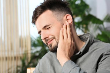 Young man suffering from ear pain at home