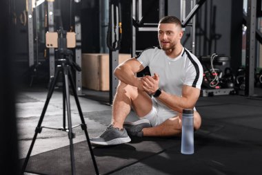 Trainer streaming online workout with phone at gym