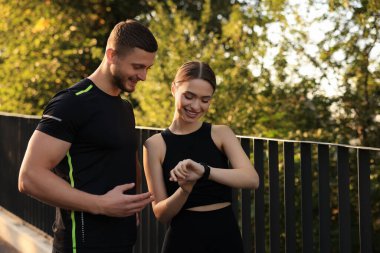 Attractive happy couple checking pulse after training in park