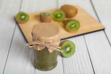 Jar of delicious kiwi jam and fresh fruits on white wooden table