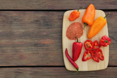 Many different peppers and spoon with spice on wooden table, top view. Space for text