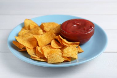 Delicious chips with ketchup on white wooden table