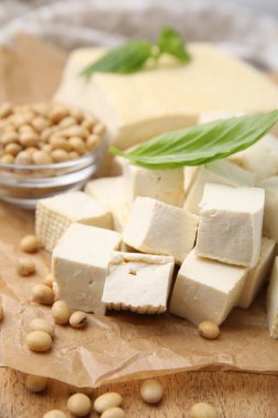 Delicious tofu cheese, basil and soybeans on wooden board, closeup