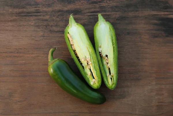 Whole and cut green chili peppers on wooden table, flat lay