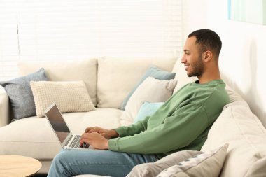 African American man typing on laptop on sofa in room