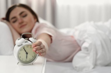 Young woman turning off alarm clock at home in morning, focus on hand. Space for text