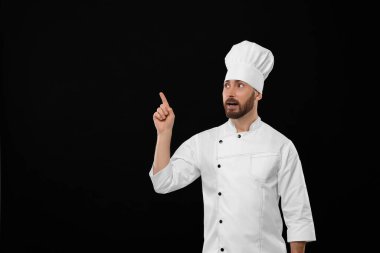 Mature chef pointing at something on black background, space for text