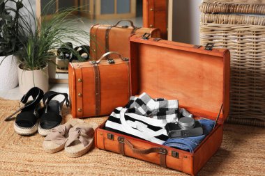 Open suitcase with folded clothes, accessories and shoes on carpet indoors