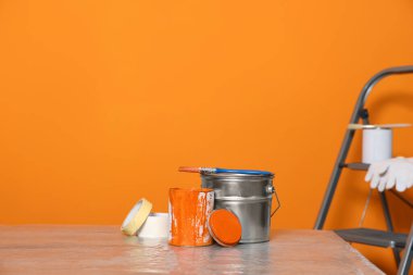 Can with paint, brush and renovation equipment on table against orange background. Space for text