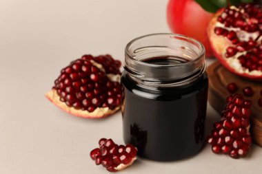 Glass jar of tasty pomegranate sauce and fresh ripe fruits on white background. Space for text