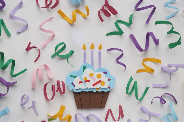 Birthday party. Paper cupcake and confetti on white background, flat lay