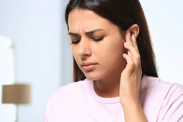 Young woman suffering from ear pain indoors, closeup