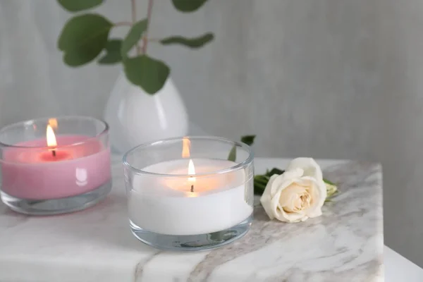 Burning candles and beautiful rose on white marble board