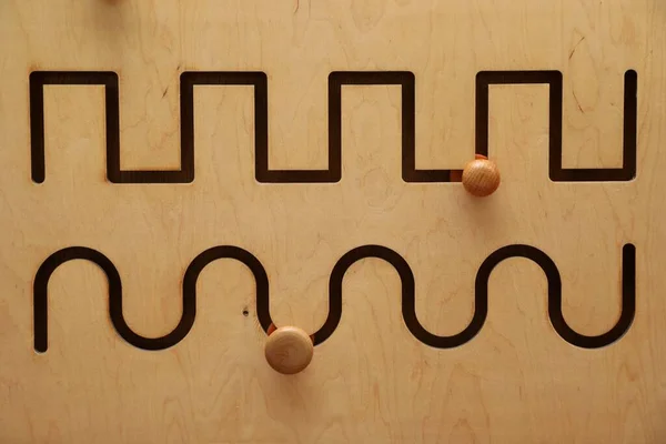 Wooden sliding maze with different lines as background, closeup. Montessori toy