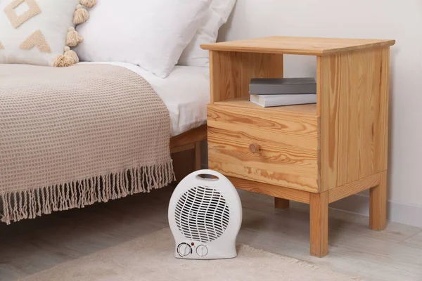 Modern electric fan heater near bedside table indoors