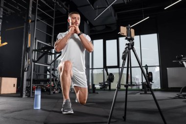 Trainer streaming online workout with phone at gym