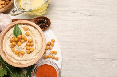 Delicious hummus with chickpeas and different ingredients on white wooden table, flat lay. Space for text