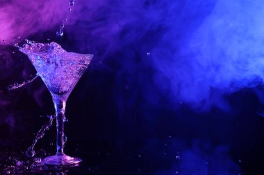 Fresh martini and splashes on mirror table in neon lights, space for text