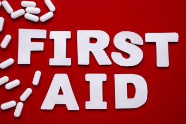 Words First Aid made of white letters and pills on red background, flat lay