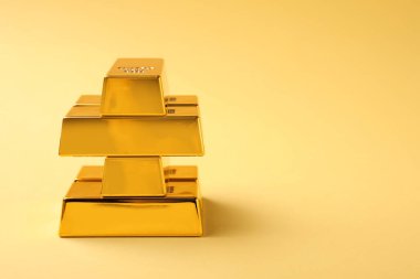 Stack of shiny gold bars on yellow background. Space for text