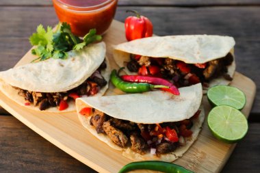 Delicious tacos with meat, vegetables and sauce on wooden table