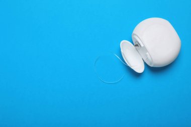 Container with dental floss on light blue background, top view. Space for text