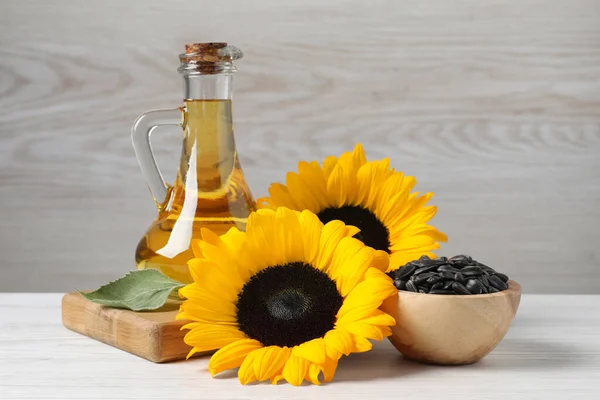 Sunflower cooking oil, seeds and yellow flowers on white wooden table