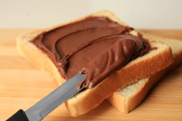 Tasty toast with chocolate paste and knife on wooden board, closeup