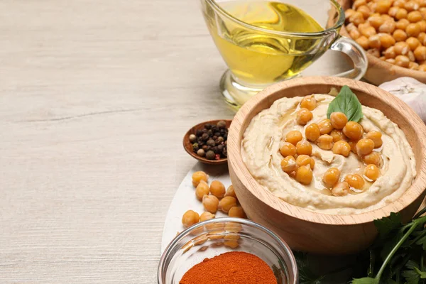 Delicious hummus with chickpeas and different ingredients on white wooden table. Space for text