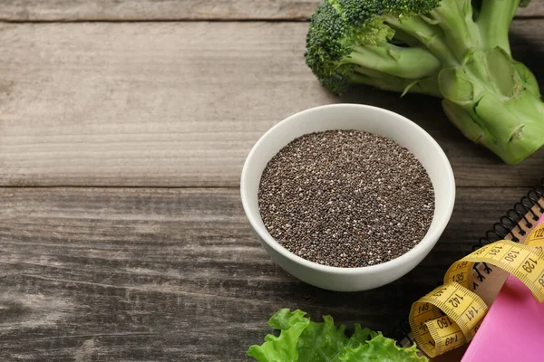 Chia seeds, measuring tape and broccoli on wooden table, space for text. Weight loss concept