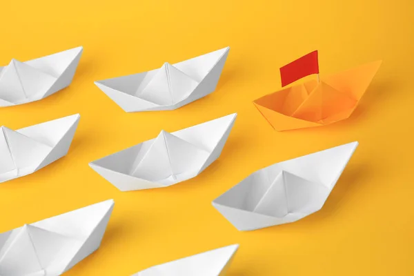 Group of paper boats following yellow one on color background. Leadership concept