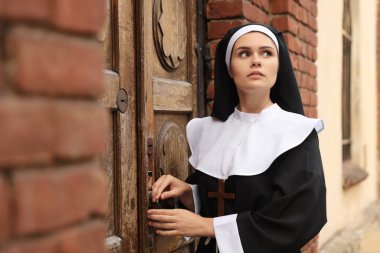 Young nun near wooden door of old building outdoors