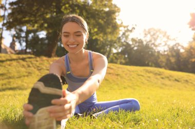 Attractive woman doing exercises on green grass in park, space for text. Stretching outdoors