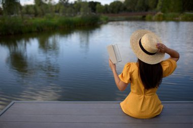 Göl kenarındaki iskelede kitap okuyan kadın.