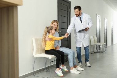 Mother and daughter having appointment with doctor. Pediatrician shaking hands with patient in clinic