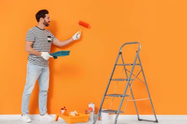 Designer painting orange wall with roller indoors