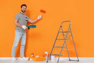 Designer painting orange wall with roller indoors